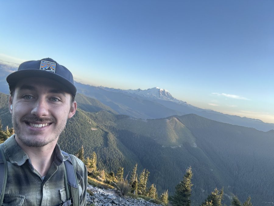 Jason, owner of Elliott Electric, on a ridge in the Cascades with Mount Rainier behind him
